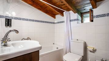 A bathroom with a sink, bathtub, toilet, and wooden ceiling beams.