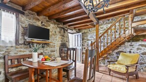 Una habitación de paredes de piedra con una mesa de madera, sillas, un televisor y una escalera.
