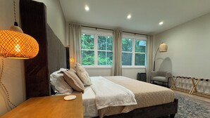 Un dormitorio moderno con cama, mesita de noche, lámpara y vistas a zonas verdes.
