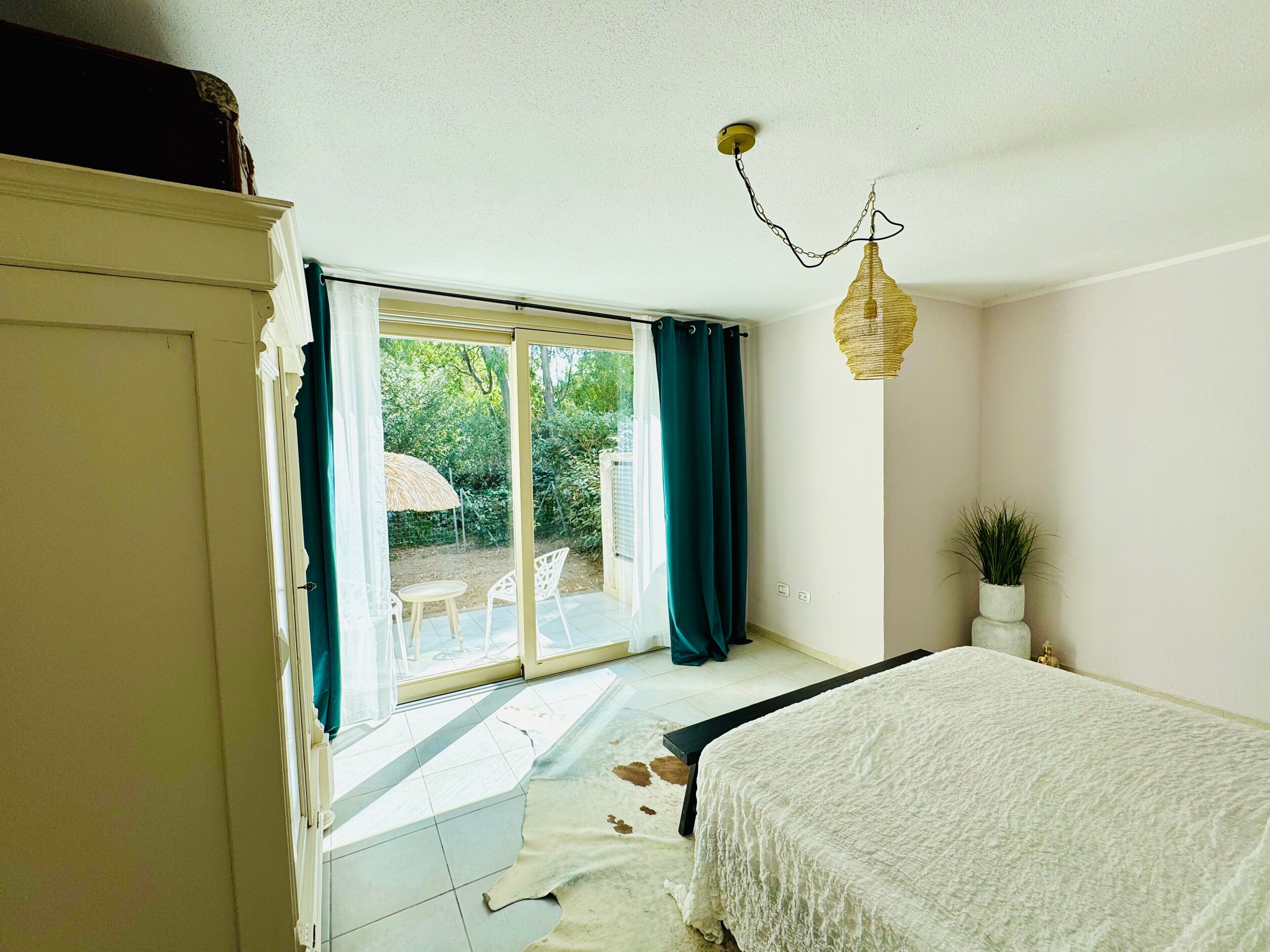 A bedroom with a bed, a sliding glass door leading to a patio, a ceiling light fixture, and a potted plant.