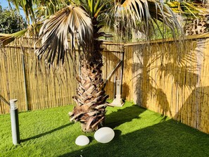 Un jardín con césped artificial, una palmera y una valla de bambú.