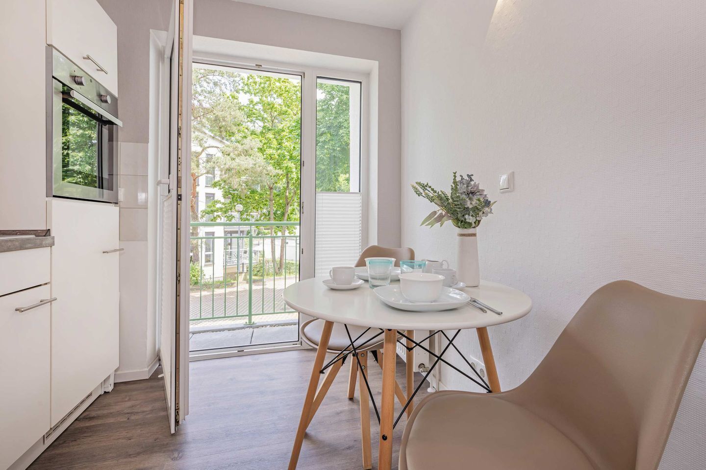 Eine moderne Küche mit Essbereich, ein Balkon mit Blick auf Grünflächen und ein mit Geschirr gedeckter Tisch.