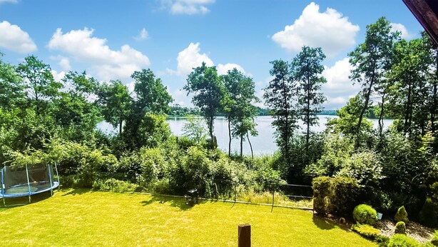 Une vue sur un lac entouré d’arbres et une zone herbeuse avec un trampoline.