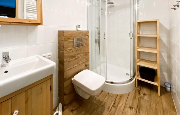A bathroom with a wooden vanity, a white sink, a toilet, a glass shower enclosure, and a wooden shelf unit.