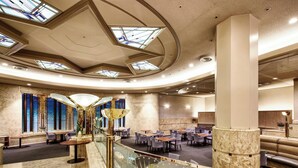 Un amplio vestíbulo de hotel con una escalera central, varias zonas de estar y tragaluces.