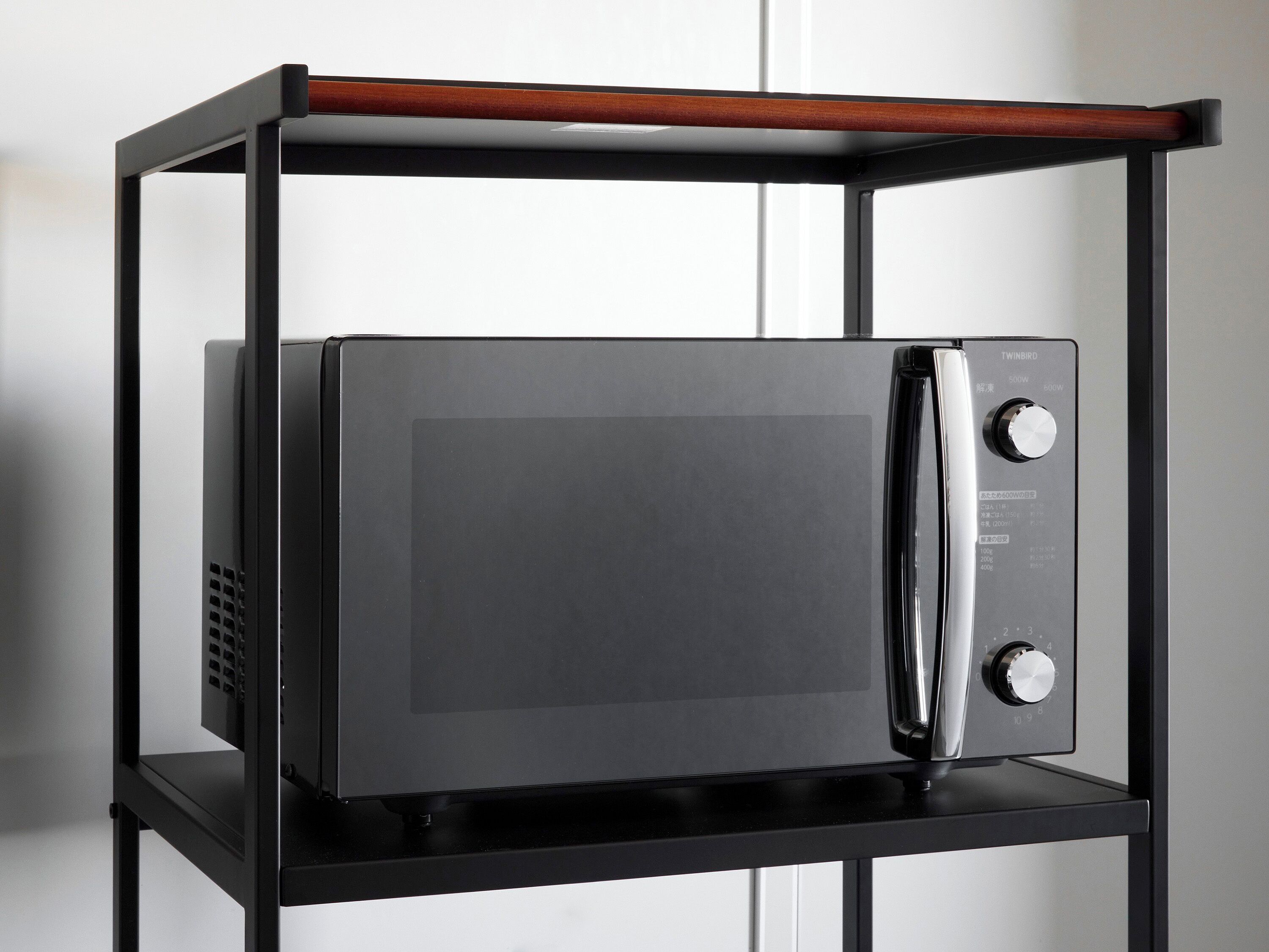 A black microwave oven on a black metal shelf with a wooden top.