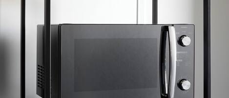 A black microwave oven on a black metal shelf with a wooden top.