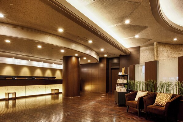 A spacious lobby with a reception desk, a large wooden pillar, and a seating area with a sofa and armchairs.
