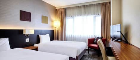 A hotel room with two beds, a desk, a chair, a TV, and a window with curtains.