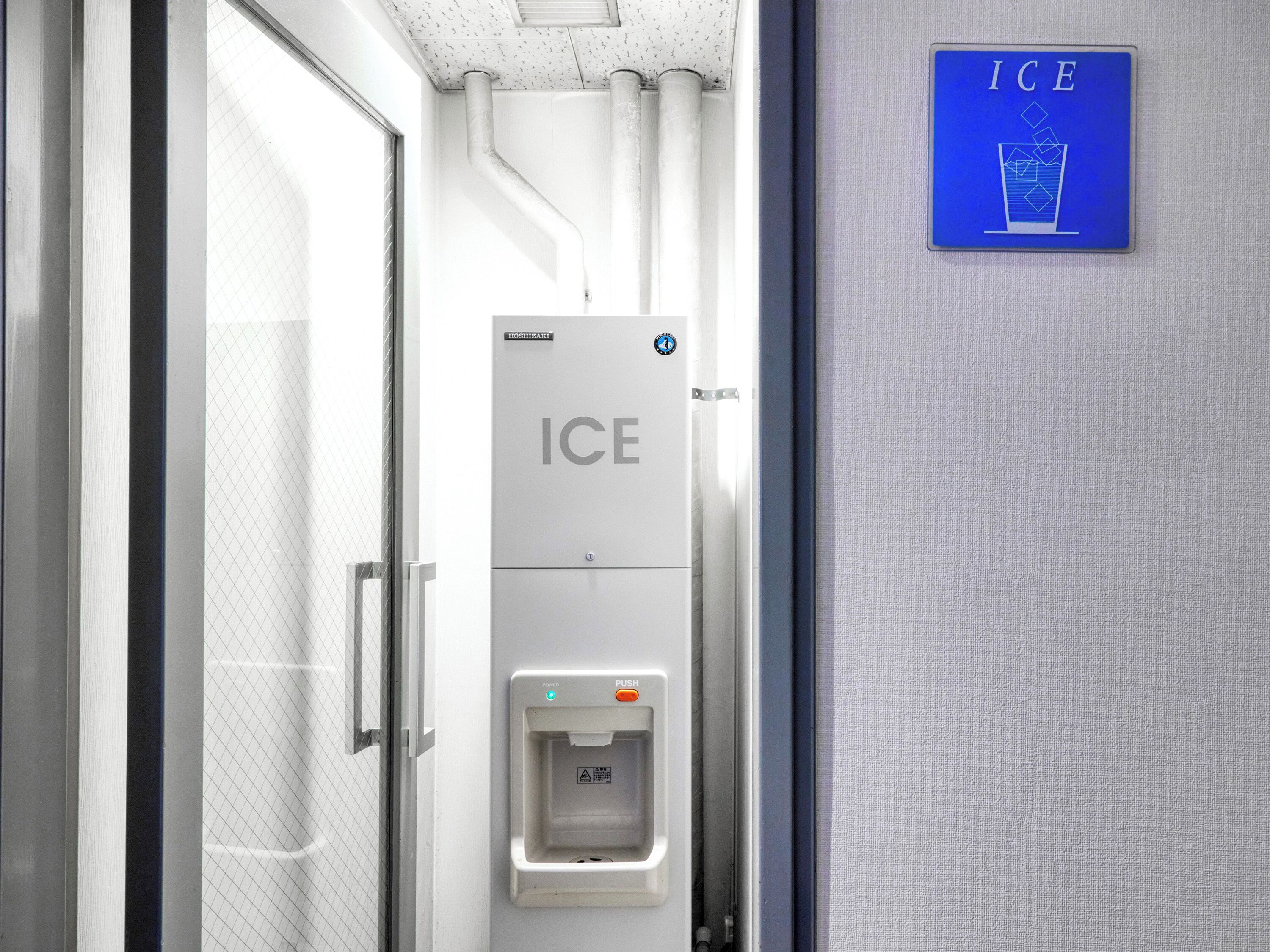 Een hotelkamer met een waterdispenser waarop 'ICE' staat en een bord dat een ijsmachine aangeeft.
