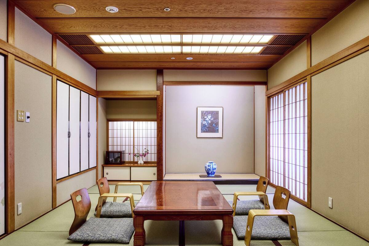 A traditional Japanese room with tatami flooring, a wooden table, and low wooden chairs.