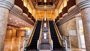 Un interior imponente con dos escaleras mecánicas que conducen a una zona central, rodeada de columnas de mármol e iluminación moderna.