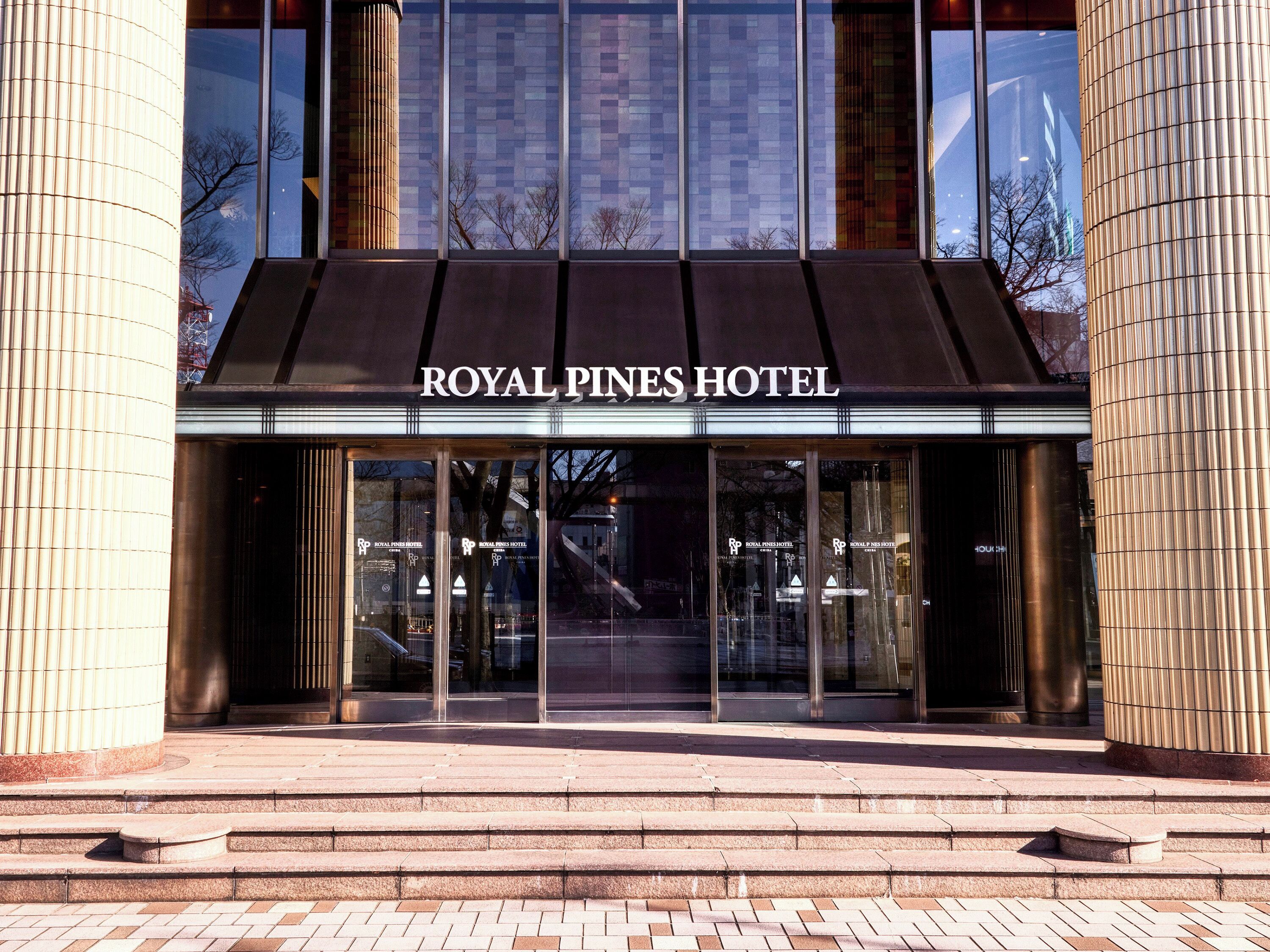 The exterior of the Royal Pines Hotel with a modern facade, large glass windows, and a prominent entrance with steps leading up to the doors.