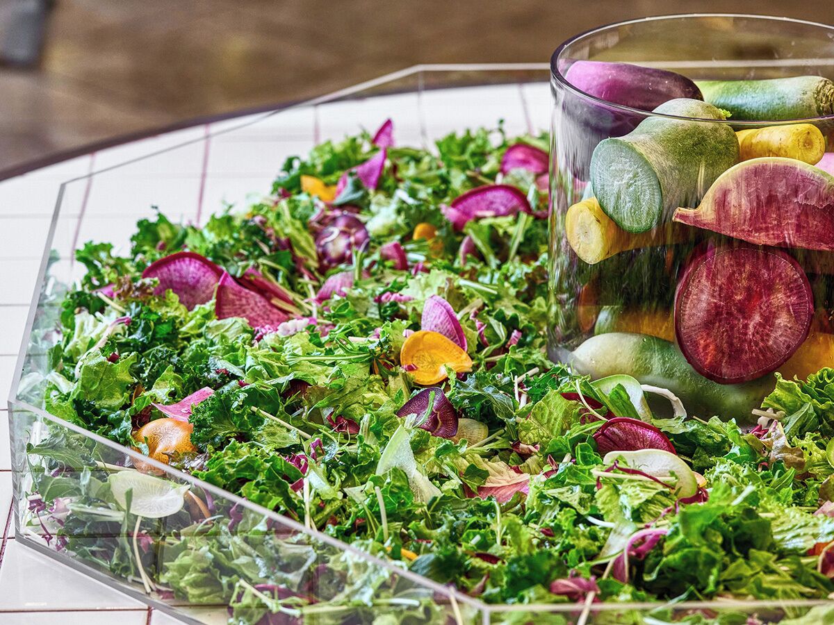 A salad with various greens and radishes in a glass container.