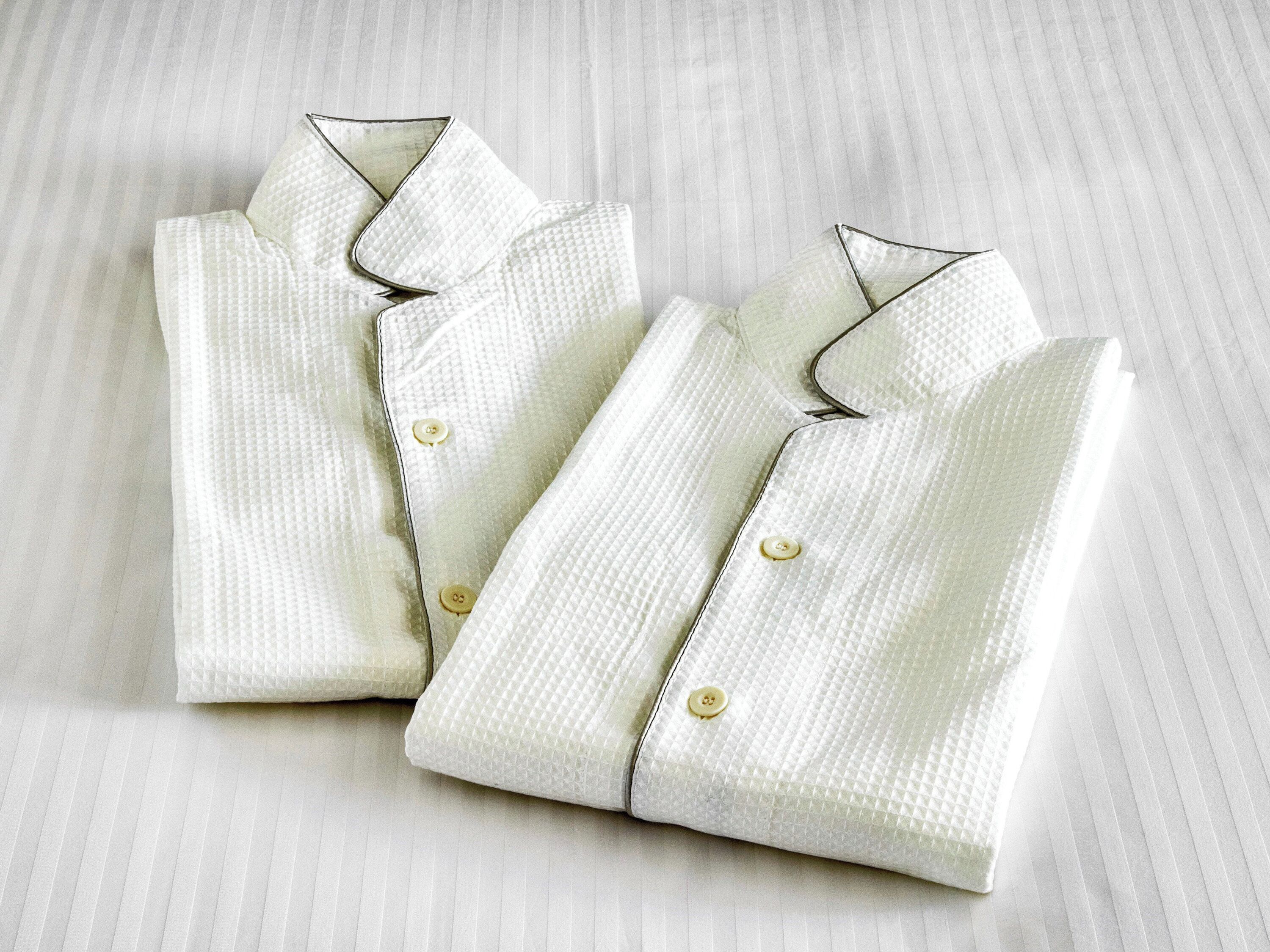 Dos camisas blancas impecablemente dobladas sobre un fondo de tela a rayas.