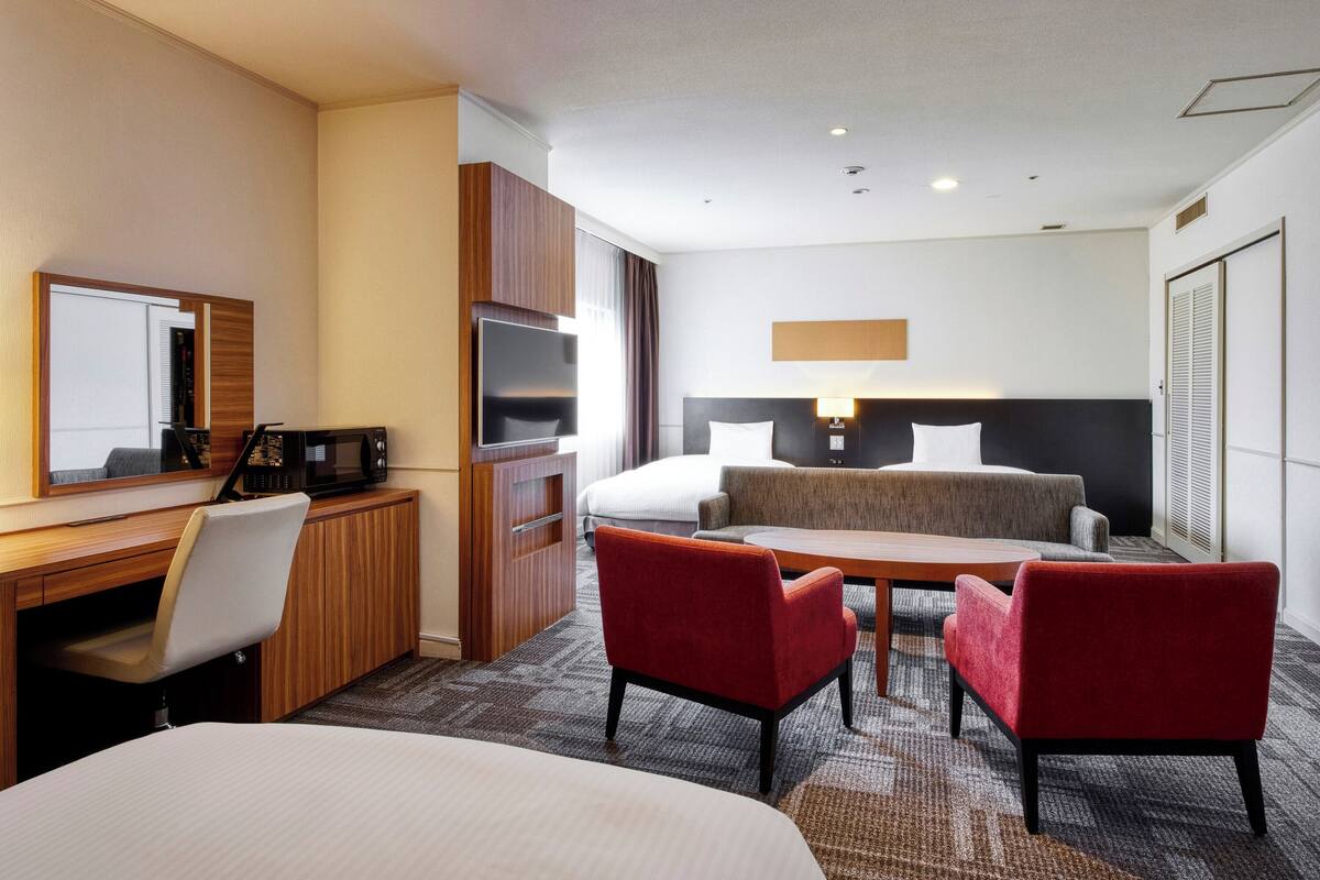 A hotel room with a bed, a desk with a computer, a TV, and a seating area with two chairs.