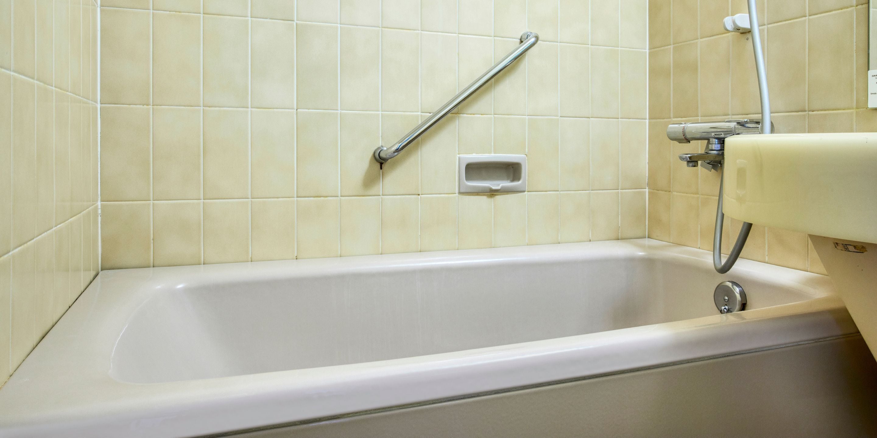 A bathroom with a bathtub, a grab bar, and a handheld showerhead.