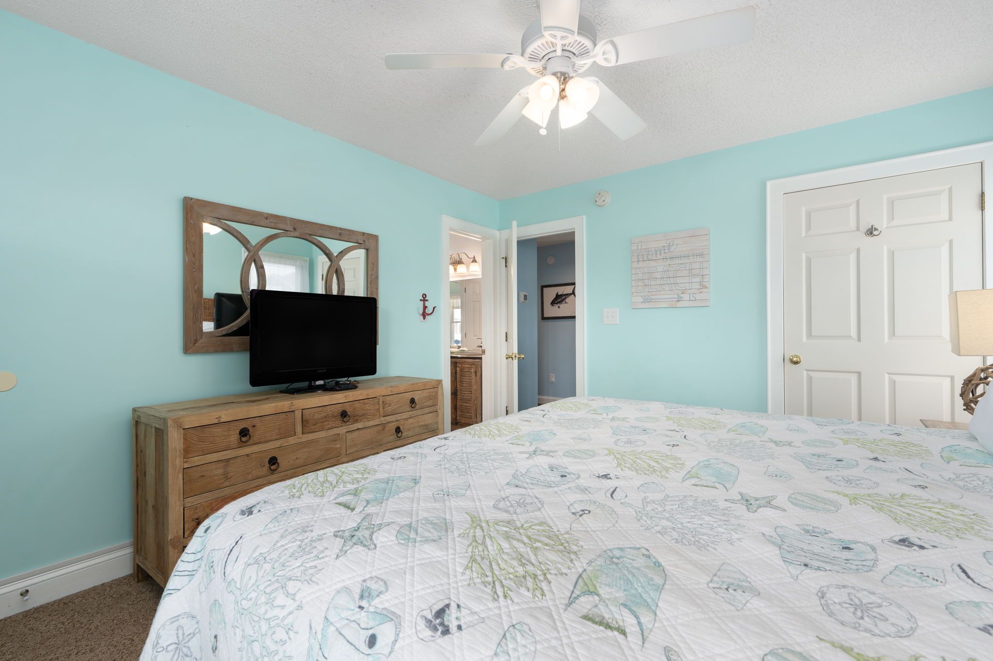 A bedroom with a bed, a dresser, a television, a ceiling fan, and a door.