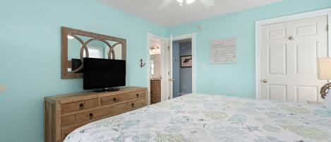 A bedroom with a bed, a dresser, a television, a ceiling fan, and a door.