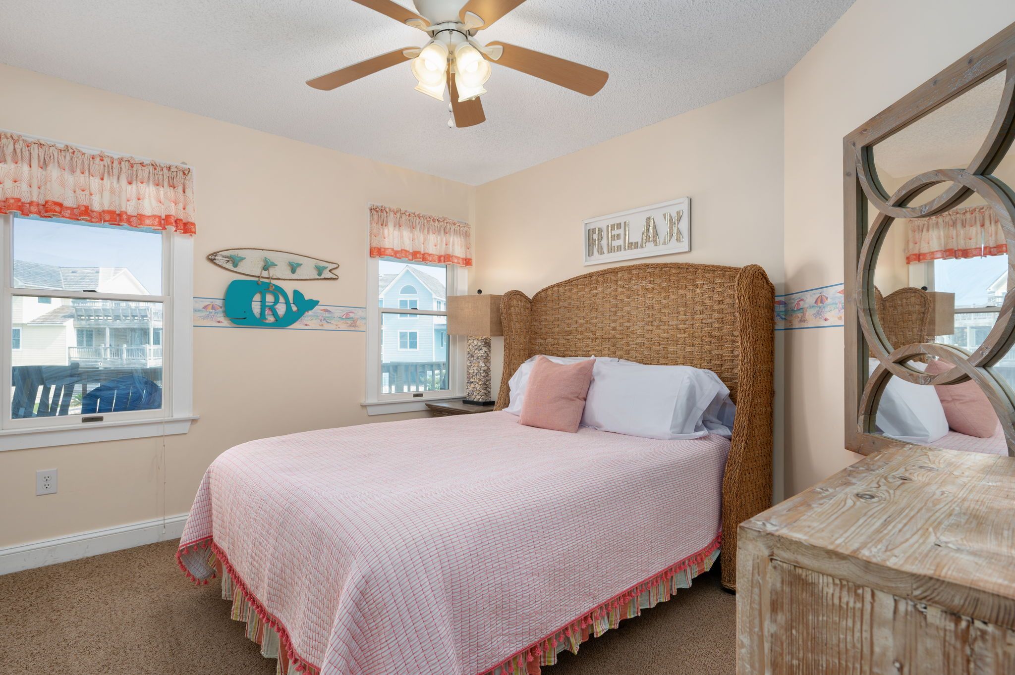 A bedroom with a bed, a ceiling fan, a window with a view, and a wall with a 'FRIENDS' sign.