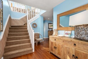 A staircase with a white railing, a wooden cabinet, and a wicker chair. - Wanderer's Rest: Oceanside, Private Pool, Hot Tub, Close to Beach! (Nags Head)