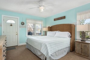 A bedroom with a bed, a ceiling fan, a window with curtains, a door, and a wall sign that reads "BEACH HOUSE". - Wanderer's Rest: Oceanside, Private Pool, Hot Tub, Close to Beach! (Nags Head)