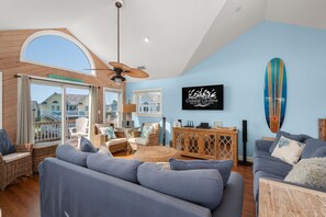 A spacious living room with a large gray sofa, wicker furniture, a ceiling fan, and a view of the outside.
