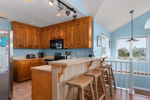 A kitchen with wooden cabinets, a microwave, a toaster, and a sink. There are wooden stools at the bar area. - Wanderer's Rest: Oceanside, Private Pool, Hot Tub, Close to Beach! (Nags Head)