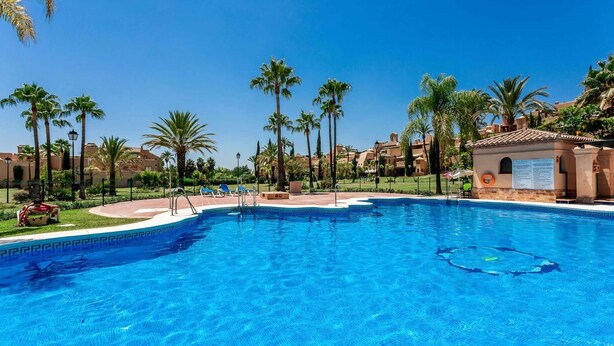 A clear blue swimming pool surrounded by palm trees and a poolside area with lounge chairs. - Splendid duplex apartment in Estepona (Estepona)