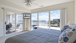 A bedroom with a large bed, a ceiling fan, a TV, and a balcony with a view of the city. - Games, Lake Views, Ease of Access to Unit & Attractions, Family-Friendly, Outdoor Comfort (Lake Ozark)