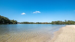 A clear view of a sandy beach with calm water and trees in the background.