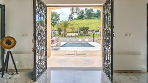 Una puerta abierta que da a un área de piscina con vistas a un jardín ajardinado.