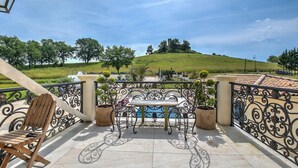 Una terraza con mesa y sillas, vista a una colina y una piscina al fondo.