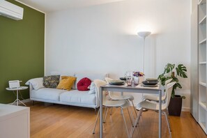 A modern living room with a white sofa, a dining table, and a potted plant. - Apartment 'Appartamento Muse' with Balcony, Wi-Fi and Air Conditioning (Trento)