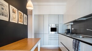 Une cuisine moderne avec des meubles blancs, un four en acier inoxydable, une table en bois et un mur noir orné de tableaux.