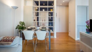 Un salon moderne comprenant un coin repas, une bibliothèque blanche et un téléviseur posé sur un meuble.