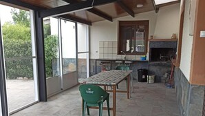 En rummelig terrasse med et bord og stole, en pejs og udsigt til grønne omgivelser.
