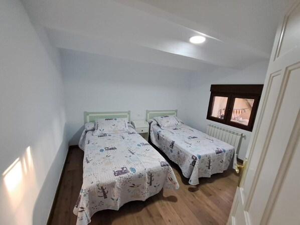 Un alojamiento pequeño con una sola habitación, dos camas individuales, un ventanal con vistas y un radiador.