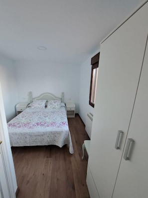 Un dormitorio con cama, mesitas de noche, armario y radiador.