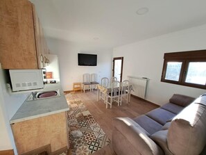 Una sala de estar con sofá, televisor, una mesa de comedor con sillas y una zona de cocina con armarios y microondas.