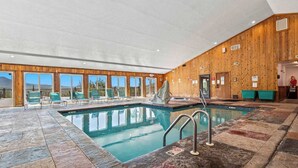 Una piscina interior con vista a las montañas, paredes de madera y sillas verdes.