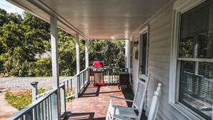 Eine überdachte Veranda mit Grill, Stuhl und Fenster.