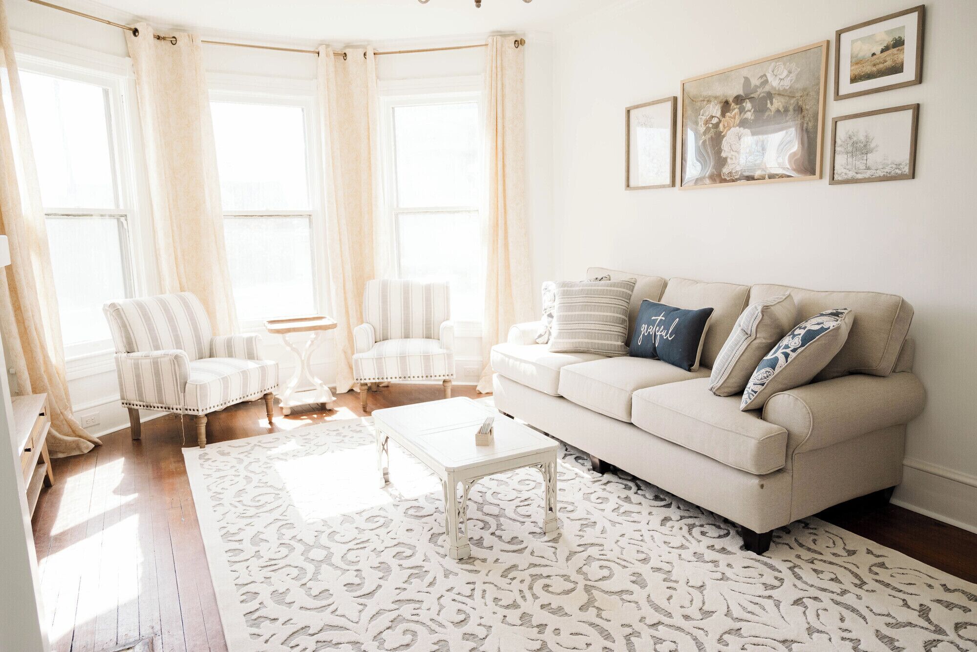 A living room with a beige sofa, striped armchairs, a white coffee table, and a patterned rug.
