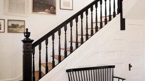Un escalier avec des balustres noires, une main courante en bois et un banc noir au pied de l’escalier.