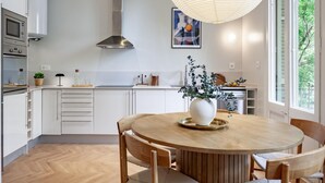 A modern kitchen with white cabinets, a stainless steel range hood, and a round wooden dining table with chairs. - Amazing views over Sagrada Familia (Barcelona)
