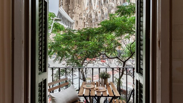 A balcony with a view of a historic building, a table with a bottle and glasses, and a bench. - Amazing views over Sagrada Familia (Barcelona)