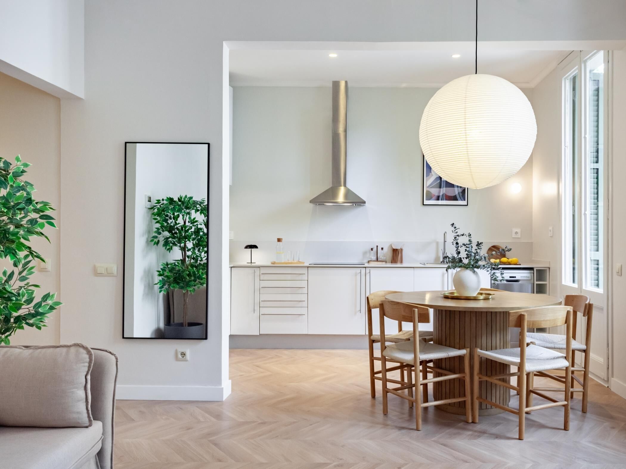 A modern kitchen with a central island, wooden chairs, and a hanging light fixture.