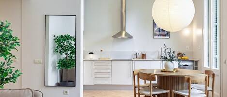 A modern kitchen with a central island, wooden chairs, and a hanging light fixture.