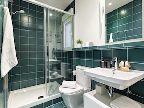 A modern bathroom with a glass-enclosed shower, a white toilet, and a sink with toiletries.