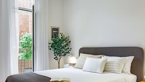 A bedroom with a bed, a bedside table, a lamp, a potted plant, and a window with curtains. - Amazing views over Sagrada Familia (Barcelona)